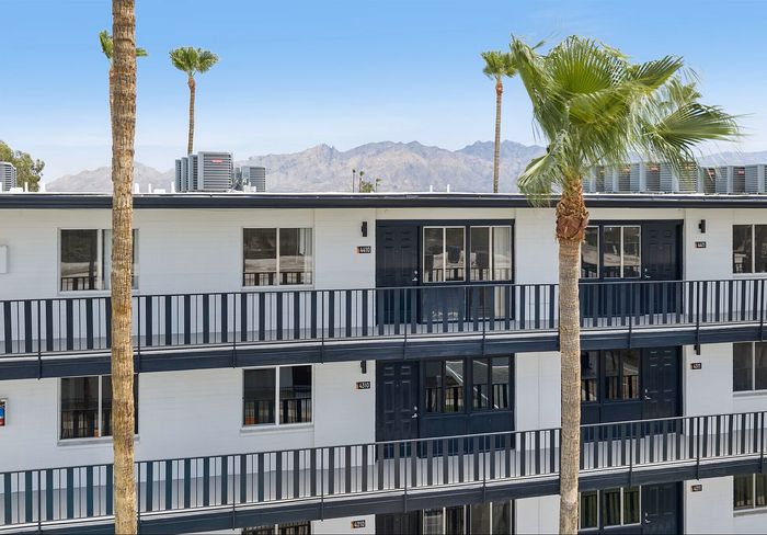Modern apartment building with mountain views, featuring sleek black railings and vibrant palm trees.