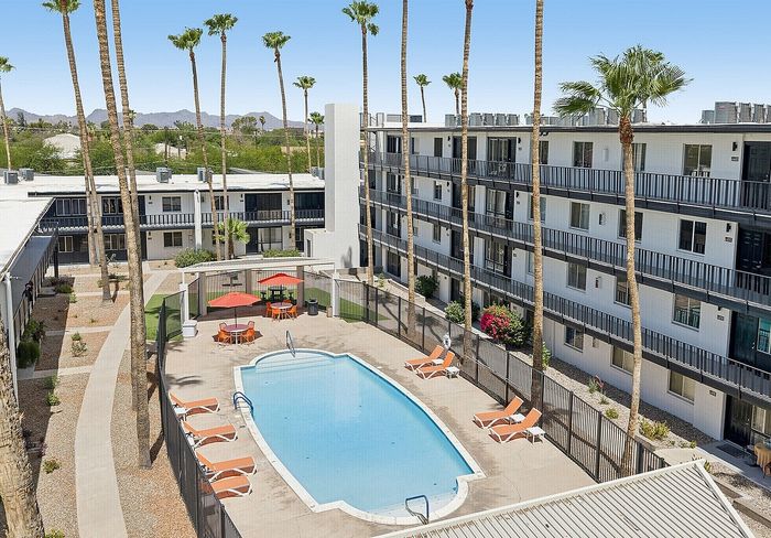 Vibrant apartment complex featuring a refreshing swimming pool, surrounded by palm trees and modern multi-story buildings, perfect for sunny relaxation.