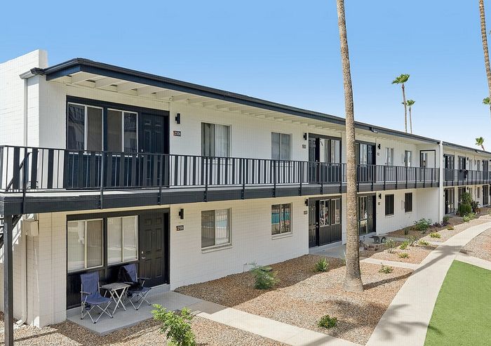 Modern apartment building with sleek balconies, surrounded by well-maintained landscaping and bright blue skies.