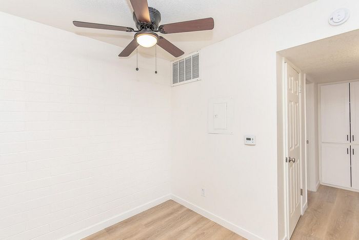 Bright and inviting room with sleek hardwood floors, modern ceiling fan, and ample natural light, perfect for a cozy living space.
