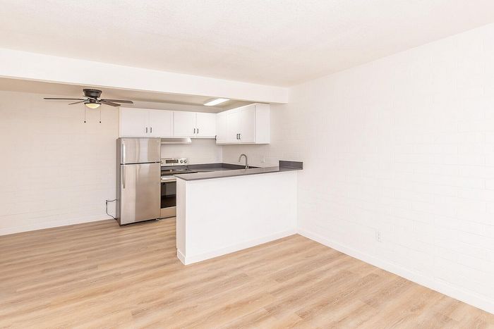 Bright, modern kitchen area featuring sleek stainless steel appliances, elegant white cabinetry, and a stylish black countertop accented by light wood flooring.