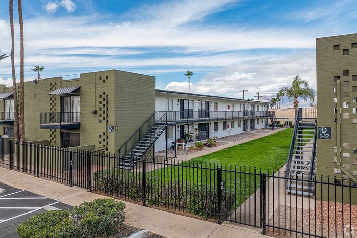 Charming apartment complex with modern design, featuring manicured green spaces and convenient outdoor stairways, set against a bright blue sky.