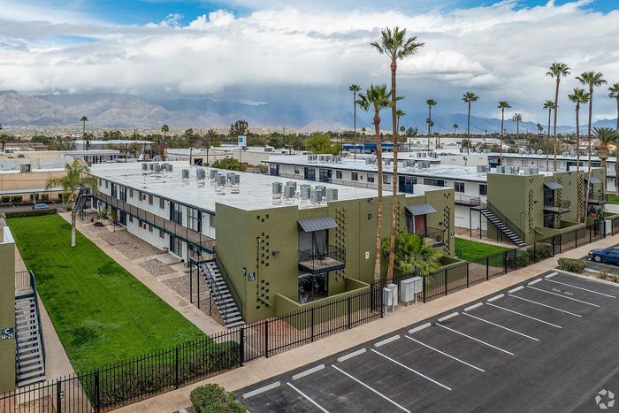 Charming apartment complex with modern green facades, lush landscaping, and majestic mountain views in the background.