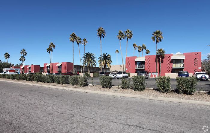 Charming apartment complex with modern red accents and lush palm trees, offering a vibrant community atmosphere.
