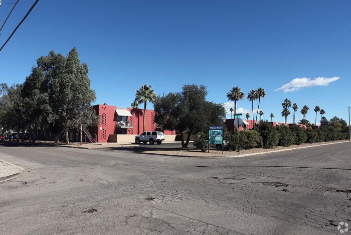Charming red apartment complex with palm trees and open sky, showcasing modern living in a serene neighborhood.