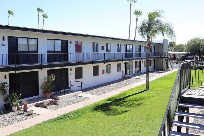 Modern apartment complex with two-story design, surrounded by lush green landscaping and tall palm trees, offering a serene and inviting living environment.