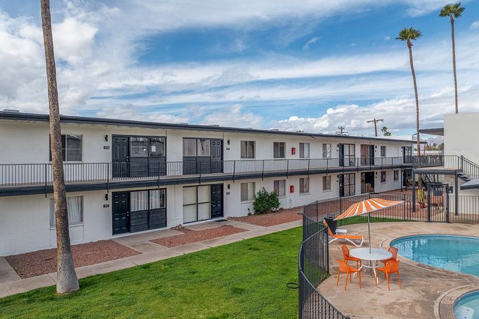 Chic apartment complex with modern charm, featuring an inviting outdoor pool and stylish seating area under a vibrant umbrella.