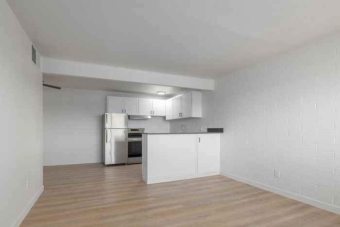 Modern open-plan kitchen with sleek white cabinetry and stainless steel appliances, complemented by stylish wood flooring.