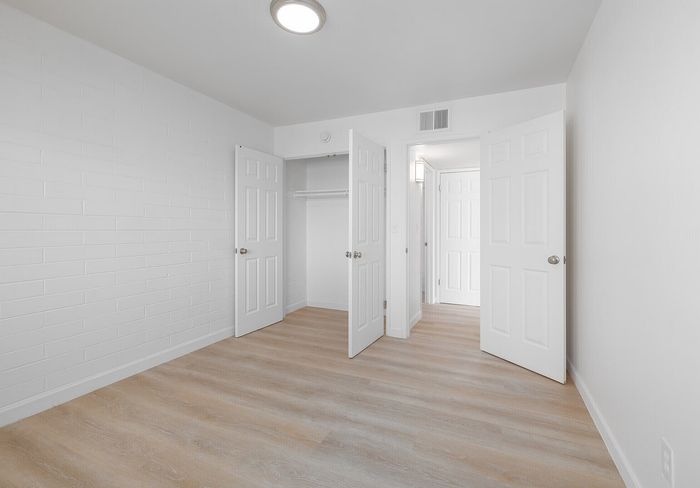 Bright, airy room featuring elegant wood flooring, stylish white doors, and an inviting open closet.