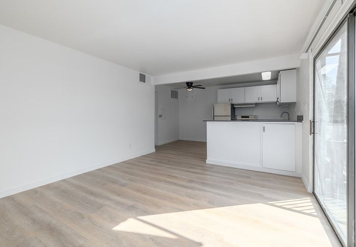 Bright, open-concept living area with sleek laminate flooring, a modern kitchen, and large sliding glass doors leading to a balcony.
