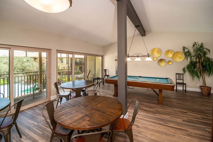 Inviting recreational room with a pool table, wooden dining tables, and large windows overlooking a lush garden view.