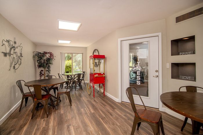 Charming communal area with round wooden tables, stylish metal chairs, and a popcorn machine, leading to an inviting fitness room.