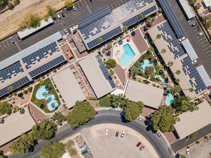Aerial view of a vibrant apartment complex with solar panels, lush greenery, and multiple inviting swimming pools.