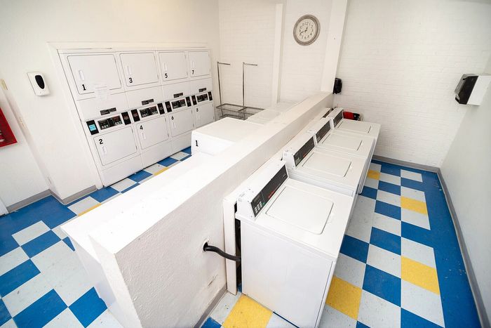 Modern laundry room with multiple washers and dryers, vibrant blue and yellow checkered flooring, and a classic wall clock.