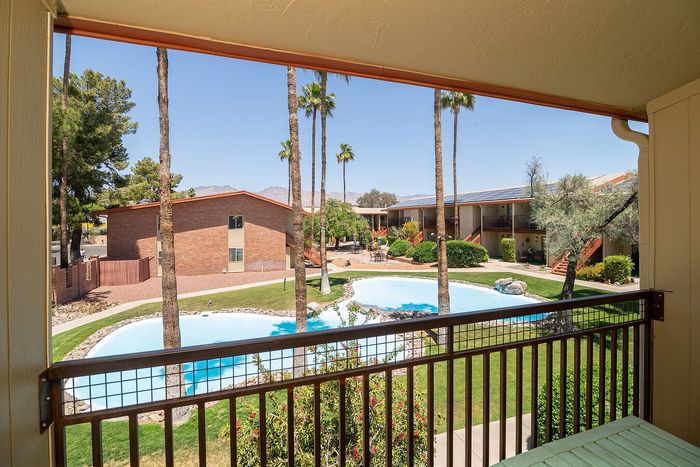 Charming apartment balcony view overlooking a serene pool area with lush landscaping and tall palm trees, perfect for relaxation and enjoying the beautiful surroundings.