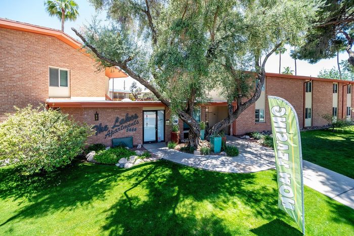 Charming brick apartment complex surrounded by lush greenery and mature trees, featuring a welcoming front entrance.