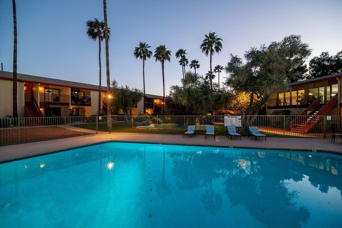 Inviting evening poolside view with shimmering water, surrounded by lush palm trees and stylish apartment buildings.