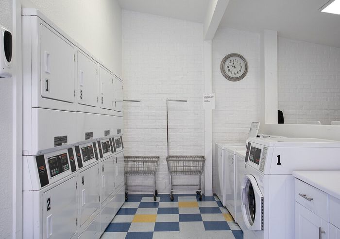 Bright and modern laundry room with stacked white washers and dryers, featuring vibrant checkered flooring and elegant white brick walls.