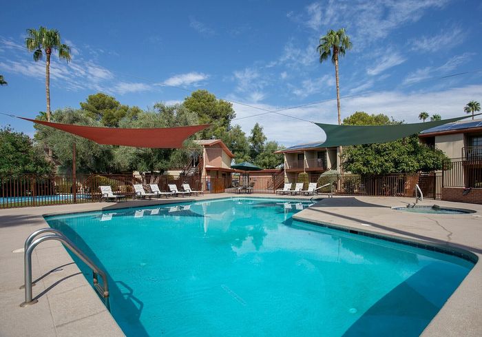 Inviting outdoor pool area surrounded by palm trees and lush greenery, featuring sun loungers and shaded cabanas, perfect for relaxation and leisure.
