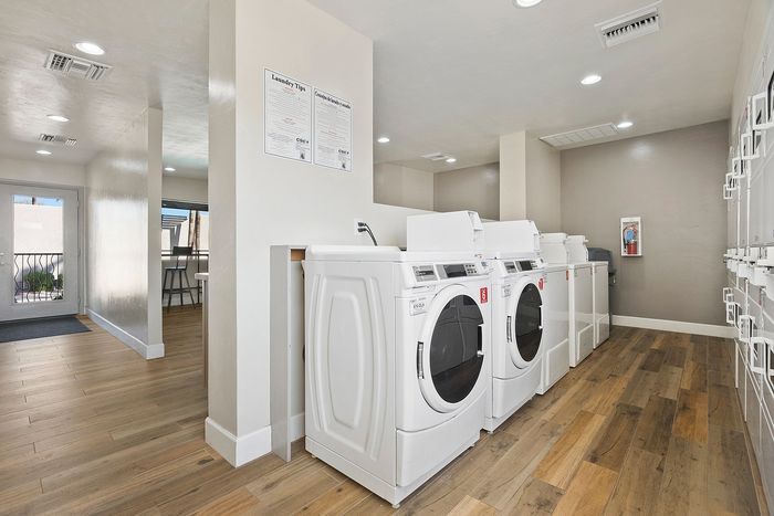 Bright and modern laundry room with multiple high-efficiency washers and dryers set against sleek wooden flooring, ideal for convenient apartment living.