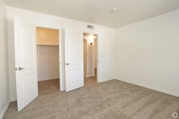 Bright and spacious room with plush carpet, featuring a large walk-in closet and stylish white double doors.