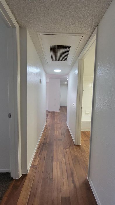 Bright corridor with elegant hardwood flooring and white walls leading to spacious, well-lit rooms.