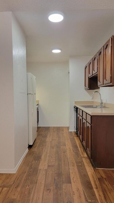 Charming kitchen with elegant wooden cabinets and sleek countertops, featuring modern lighting and a smooth wood-style floor.