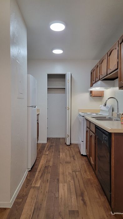Charming galley kitchen with warm wooden cabinetry, sleek countertops, and modern appliances, complemented by elegant hardwood flooring and ambient ceiling lights.