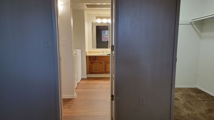 Bright hallway leading to a cozy bathroom with warm wooden cabinetry and sleek countertops, adjacent to a spacious walk-in closet.