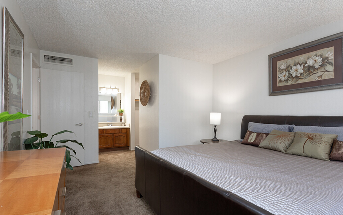 Elegant bedroom showcasing a cozy bed with stylish bedding, a wooden dresser, and an en-suite vanity area with modern lighting.