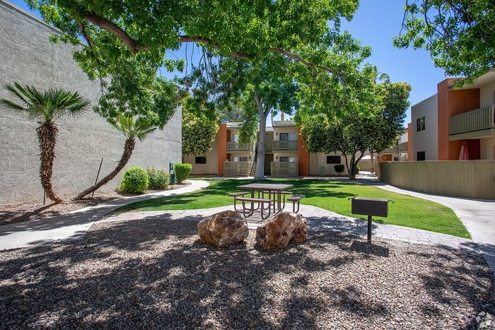 Beautiful apartment courtyard with lush green lawn, mature trees, picnic area, and charming pathway.