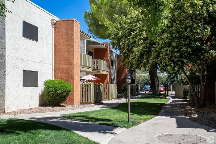 Beautiful apartment courtyard with lush green lawn, mature trees, picnic area, and charming pathway.