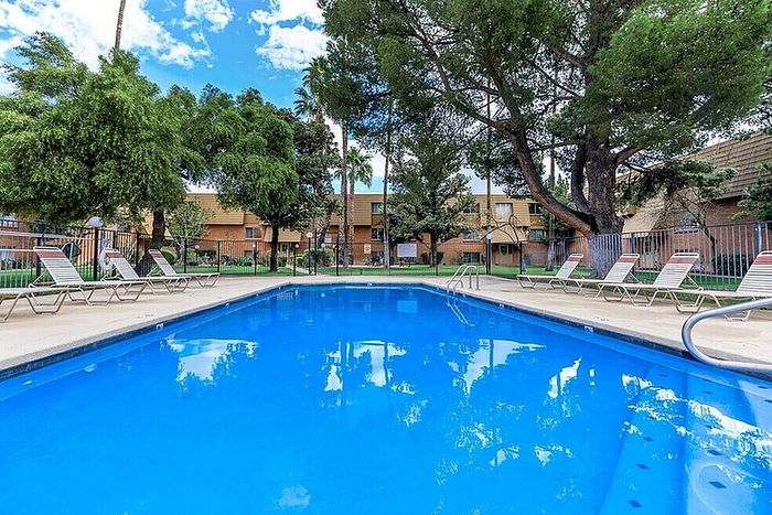 Inviting apartment complex with a sparkling blue pool, surrounded by lush greenery and comfortable lounge chairs for relaxation.