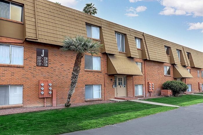 Charming brick apartment complex with unique architectural design, featuring lush green landscaping and tall palm trees.