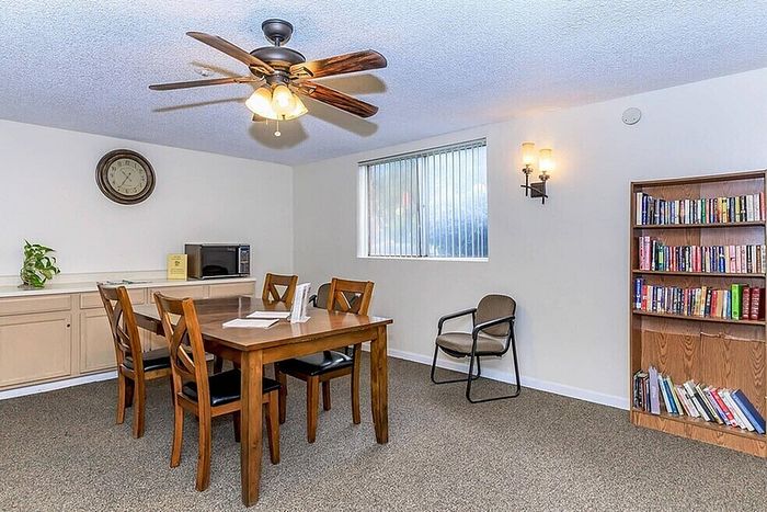 Inviting dining room with a cozy ambiance, featuring a wooden table set, ceiling fan, and a stylish bookshelf.