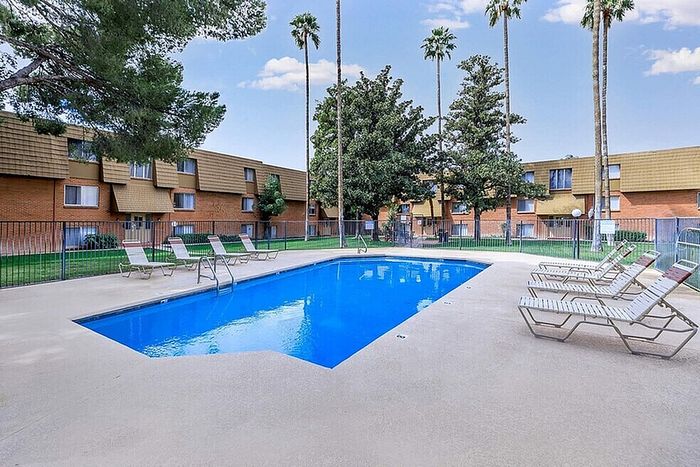 Inviting outdoor pool area with stylish lounge chairs, surrounded by lush greenery and modern apartment buildings for a serene living experience.
