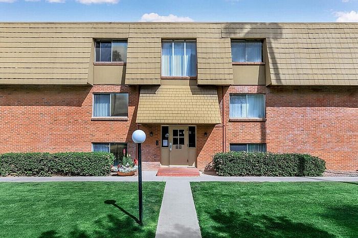 Charming brick apartment building with modern windows and a well-maintained front lawn, offering a welcoming entrance and serene atmosphere.