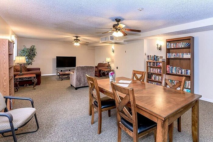 Inviting living room with plush seating, elegant wooden dining table, ceiling fans, and extensive bookshelf, perfect for relaxation and entertainment.