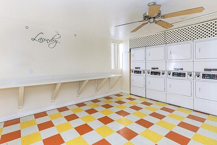 Bright and functional communal laundry room featuring modern washing machines, ample folding space, and vibrant checkerboard flooring.
