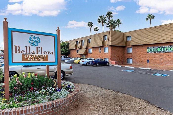 Inviting Bella Flora Apartments showcasing modern design with ample parking, vibrant flower beds, and palm trees under a clear sky.