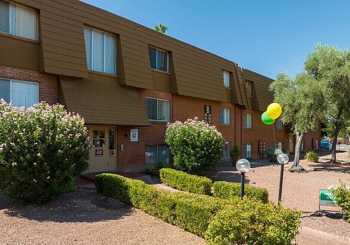 Charming apartment complex with inviting landscaped entrance, vibrant balloons, and lush greenery.