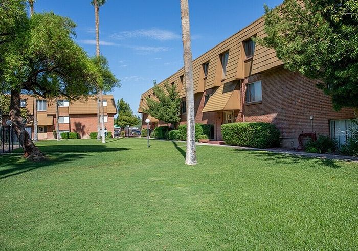 Charming apartment complex with lush green lawns and mature trees under clear blue skies.