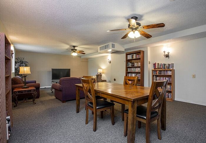 Cozy living and dining area with stylish wooden furniture, ceiling fans, and a well-stocked bookshelf in a spacious apartment.