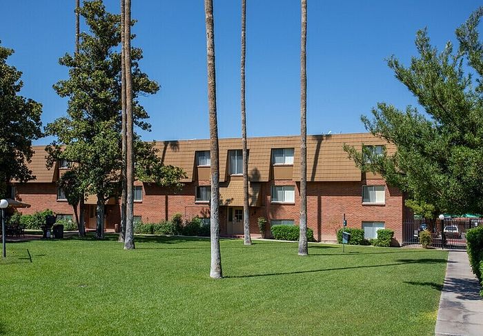 Charming brick apartment building with lush green lawn and tall palm trees under a clear blue sky.