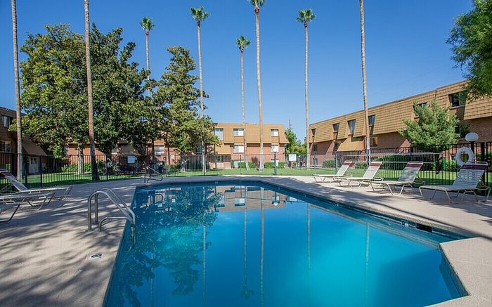Inviting outdoor pool area surrounded by lush greenery and tall palm trees, perfect for relaxation in a tranquil apartment complex setting.