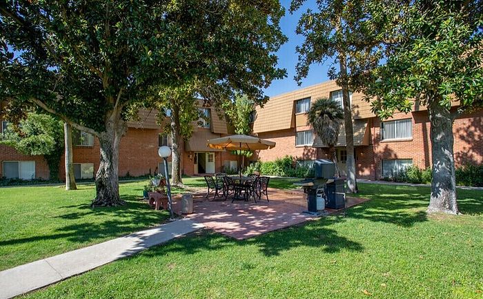 Charming apartment exterior with a lush green courtyard featuring outdoor dining area and BBQ under the shade of trees.