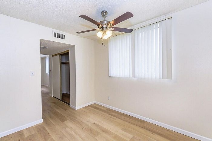 Bright and airy room with sleek wooden flooring, ceiling fan, and ample natural light from large windows.