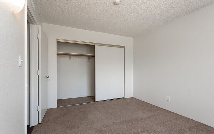Bright and airy bedroom with neutral walls, plush carpeting, and a spacious closet for comfortable living.