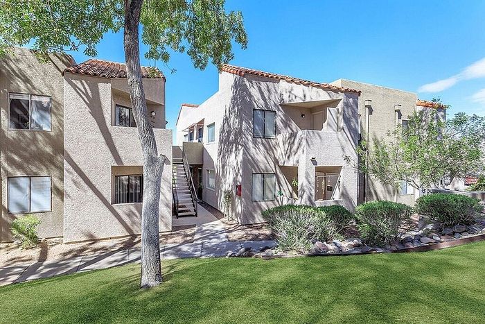 Charming apartment complex with a modern exterior, featuring lush landscaping and a welcoming entrance under a clear blue sky.
