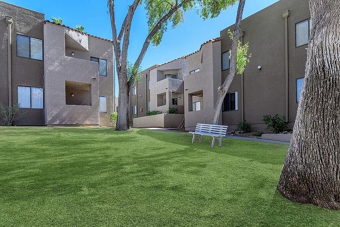 Serene apartment complex with lush green courtyard and inviting bench, surrounded by modern architecture.